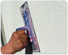 Stukadoor werkt met een pleisterspaan aan een wand met structuurpleister
