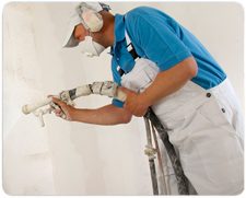 Vakman spuit machinaal spackpleister op een plafond, met stofmasker en spuitpistool
